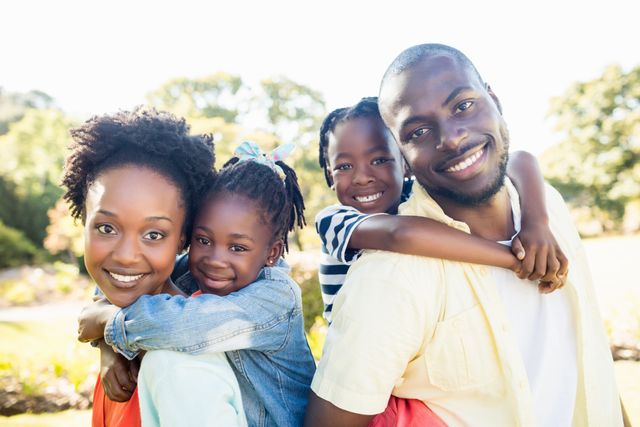 African American family of four enjoying a sunny day at a park. Parents and children smiling and bonding. Suitable for family-oriented campaigns, advertisements, and articles focusing on family values, outdoor activities, and parent-child relationships.