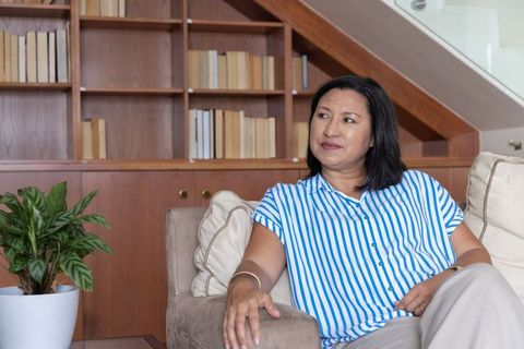 Mature woman relaxing on beige sofa in contemporary living room with bookshelf and staircase