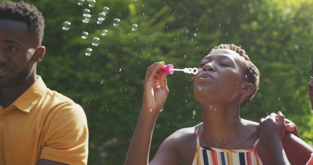 Happy african american couple standing in garden and blowing bubbles together. Lifestyle and domestic life.