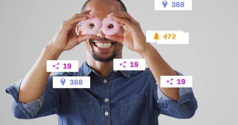 Playful man holding donuts as goggles with floating social media icons