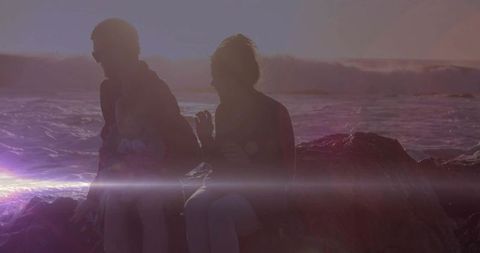 Silhouetted Family Relaxing On Coastal Rocks During Sunset