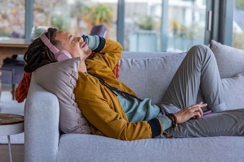 African american man relaxing on couch listening to music with pink headphones at home