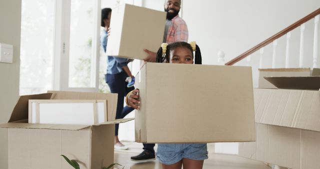 African American family carrying cardboard boxes into new home. Child smiling and helping with unpacking. Perfect for themes related to moving house, family togetherness, relocation, and home improvement.