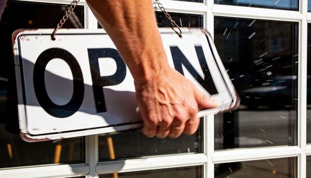 Sunlit Hand Holding OPEN Sign on Multi-Panel Glass Door, Motion Blur and Reflections