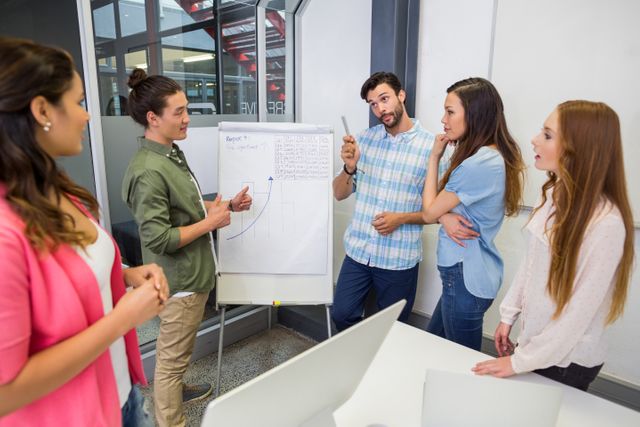 Group of young professionals engaged in a strategic discussion around a flip chart in a modern office. Ideal for use in business presentations, corporate training materials, teamwork and collaboration themes, and articles about office culture and professional development.
