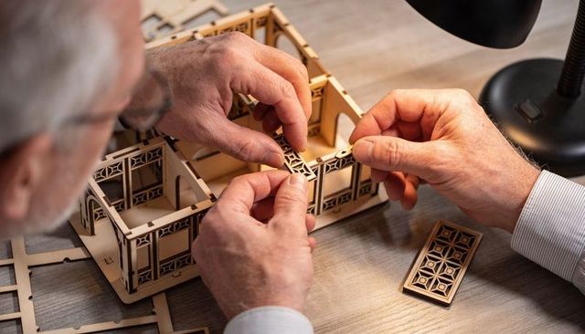 Senior hands assembling laser-cut wooden architectural model with decorative lattice panels