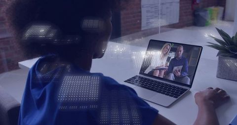 Joining virtual meeting on laptop in modern loft workspace with holographic data overlay