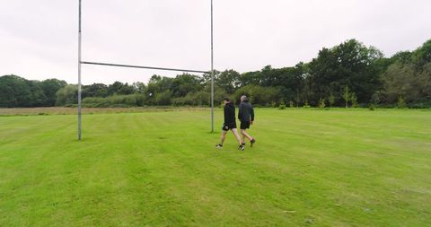 Two People Strolling on Grassy Field Near Goalpost
