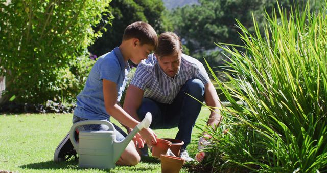 This photo depicts a father and son engaged in gardening outdoors on a sunny day. The father is helping his son with planting, demonstrating a shared family activity and bonding time. This can be used for parenting blogs, gardening websites, family lifestyle articles, or advertisements promoting outdoor activities or family products.