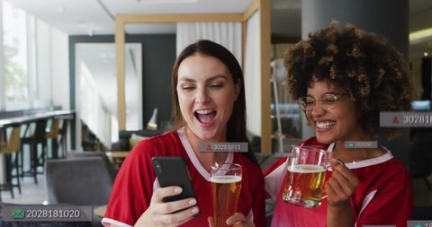 Two diverse women are laughing and enjoying mugs of beer, showcasing a friendly and joyful atmosphere in a modern bar. Digital overlay icons suggest social media engagement or digital communication, adding a contemporary touch. Perfect for concepts related to friendship, celebration, social gatherings, digital interaction, and cheerful, relaxed moments.