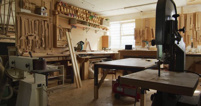 Carpenter's workshop showcasing various tools, a bandsaw, and workbenches bathed in natural light. Suitable for articles or advertisements about woodworking, carpentry tools, artisanal craftsmanship, do-it-yourself projects, and workspaces.