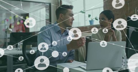 Colleagues collaborating over laptop with digital network overlay in modern brick office