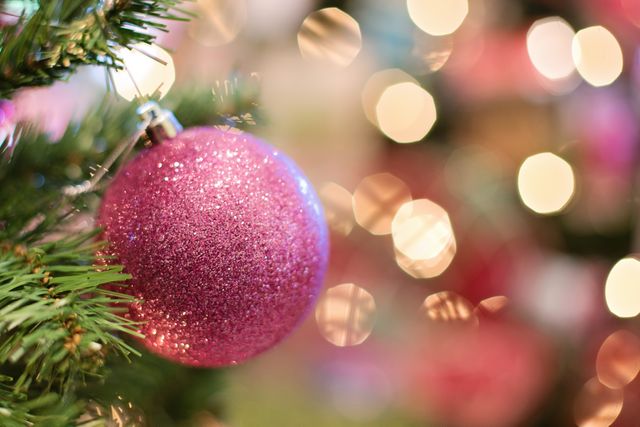 Perfect for holiday-themed content, this sparkling pink Christmas ornament adds a festive touch. The bokeh lights in the background create a cozy, warm atmosphere, ideal for use in holiday cards, seasonal advertisements, or decorating inspiration guides.