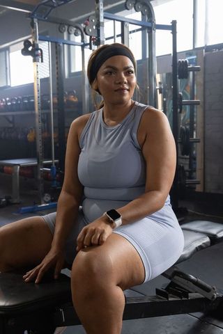 African american woman sitting on weight bench after strength workout wearing smartwatch