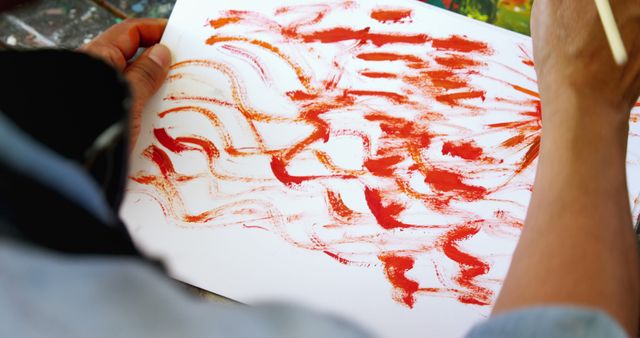 An individual is creating an abstract red painting on paper, with copy space. Artistic expression is captured as the person uses bold strokes to convey creativity and emotion.