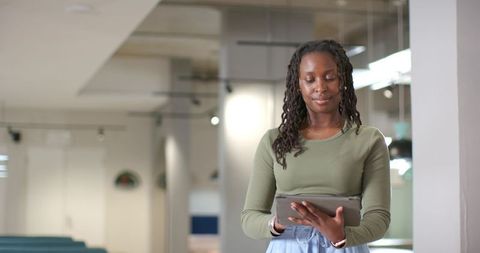 African woman using tablet in modern coworking space, calm focused professional, wearing olive top