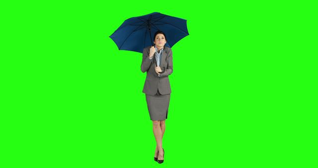 Professional woman in business attire holding a blue umbrella, standing against a green screen background. This image is perfect for advertisements, presentations, or digital media that require easy background removal or chroma keying to insert the subject into various contexts.