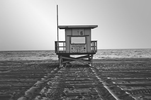 Lifeguard tower on an empty beach with ocean in the background, in black and white. Shows quiet, serene coastal scenery, sense of solitude, and calm. Ideal for use in travel blogs, articles on coastal life, beach safety, or conceptual pieces on peace and solitude.