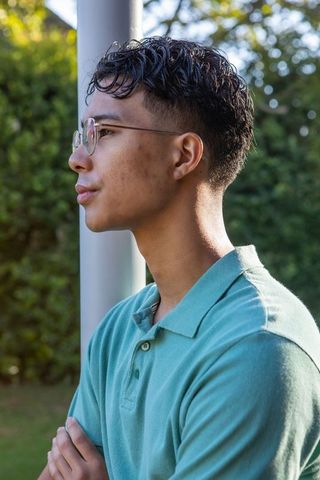 Young Man Reflecting in Garden with Teal Polo and Glasses