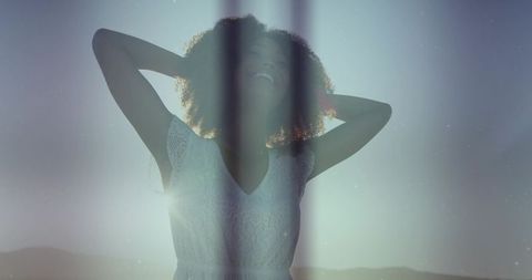 Backlit woman standing with hands behind head smiling in white lace dress at sunset
