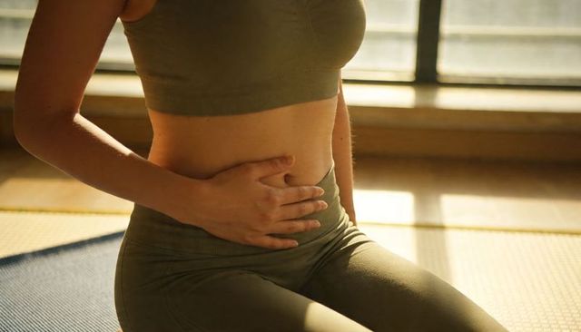 Sunlit yoga core breathing practice with woman holding abdomen on mat in olive activewear