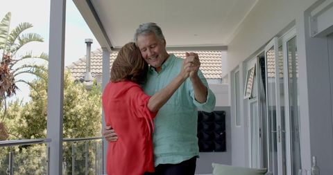 Smiling senior couple dancing on sunny balcony