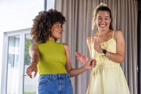 Diverse friends singing and laughing using broom-handle microphone in sunlit living room