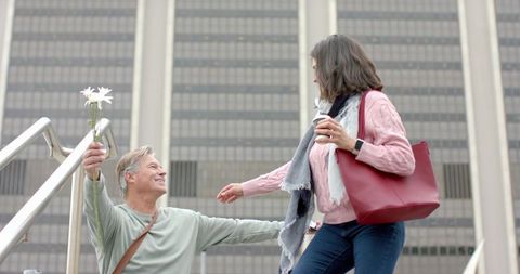 Mature couple showing affection: man offering daisies while woman holds coffee on stairs