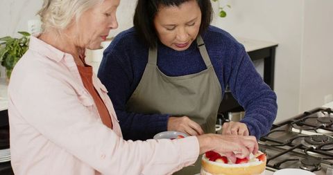 Diverse Women Decorating Sponge Cake with Strawberries at Home