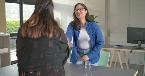 Female coworkers shaking hands in bright modern office during casual meeting