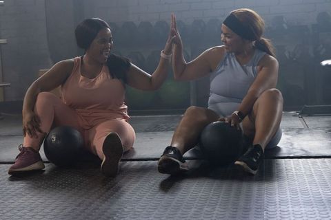 African american women high-fiving while resting with medicine balls during workout