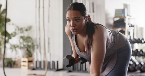 African american woman performing bent-over dumbbell row in gym building strength