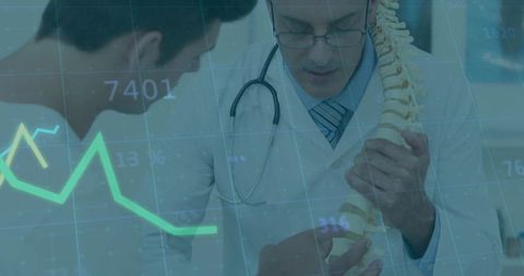 Doctor consulting patient with spine model while overlaying digital charts and analytics