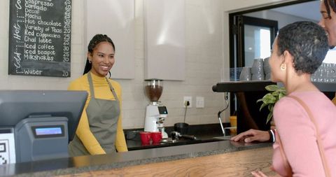 Smiling barista serving customers at modern coffee counter with pos and espresso machine