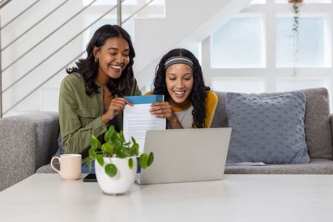 Mother and daughter celebrating acceptance letter while using laptop on cozy sofa