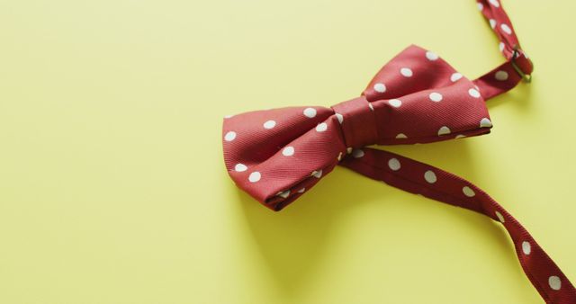 This image of a red dotted bow tie centered on a vibrant yellow background can be used in various ways. It is ideal for fashion websites aiming to highlight men's accessories, online stores selling bow ties, and social media campaigns promoting formal wear. Additionally, it is perfect for blog posts discussing men's fashion trends, stylist portfolios, and print advertising materials focusing on elegant and stylish men's clothing themes.