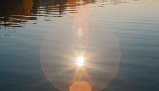Sun reflecting on calm lake casting geometric lens flare, amber ripples and soft glow