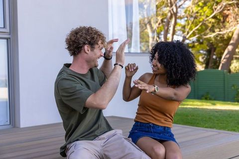 Interracial couple high-fiving on wooden deck relaxing together in sunny backyard lifestyle