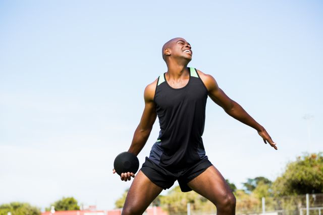 Young male athlete in black sports attire preparing to throw discus at outdoor stadium. Perfect for illustrating athletic training, sports competitions, fitness exercises, and motivational sports moments.