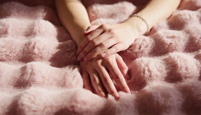 Resting hands on pink faux-fur blanket wearing beaded bracelet, soft plush texture closeup