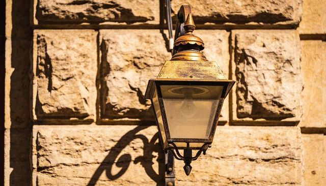 Antique brass lantern casting sculpted shadow on sunlit stone facade