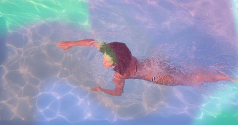 Overhead swimmer gliding through pool with teal to purple caustic soft light and splashes