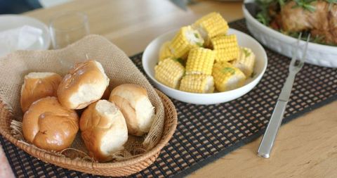 Wicker basket holding soft dinner rolls with buttered corn on rustic wooden table