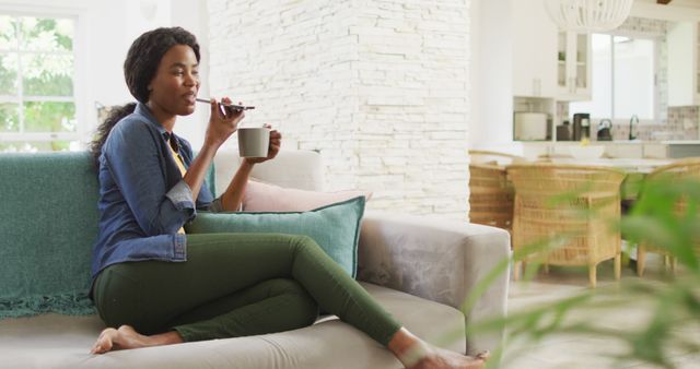 Image of happy african american woman on sofa using smartphone. leisure and relax, spending free time with technology at home.