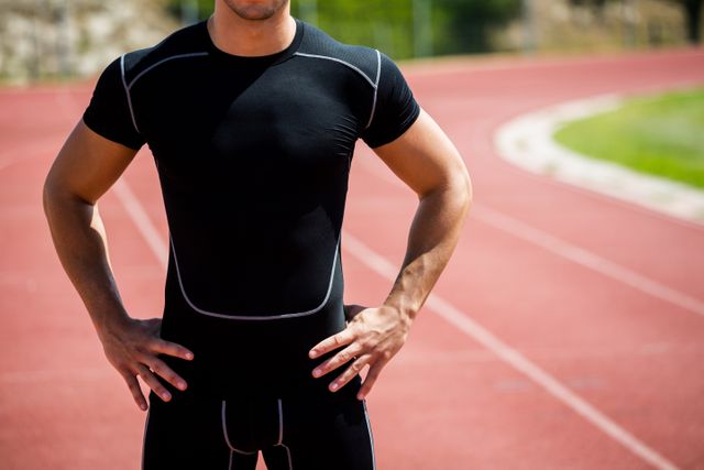 Mid section of athlete standing with hands on hip on running track