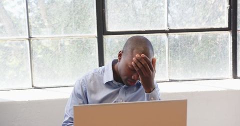 Stressed Businessman Working on Laptop by Office Window