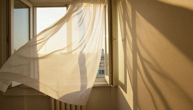 Billowing sheer curtain casting golden rooftop shadows through open casement window