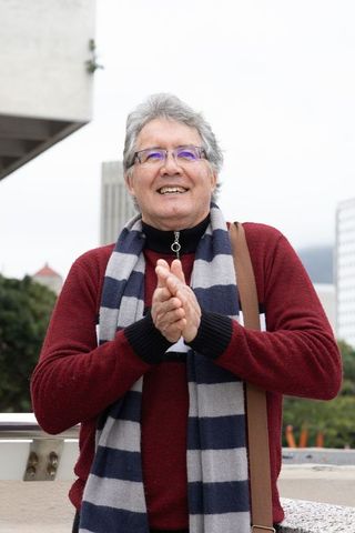Senior man clapping on urban terrace wearing red sweater striped scarf eyeglasses smiling