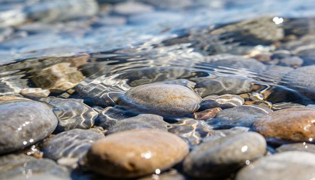 Crystal clear shallow water revealing smooth river pebbles with shimmering ripples