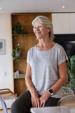 Senior woman wearing smartwatch sitting on countertop in modern open-plan living room
